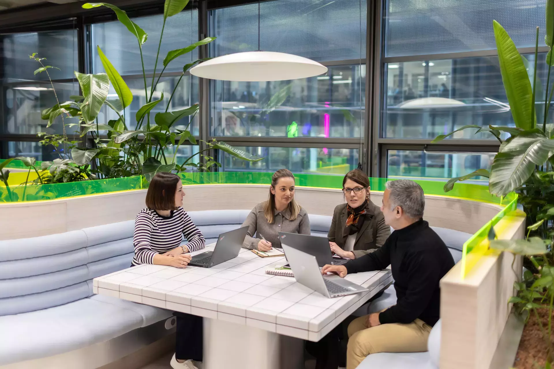 people_colleagues_talking_sitting_on_laptops_in_communal_area